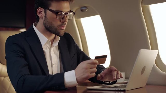businessman using laptop and holding credit card while traveling by plane
