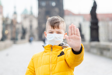 Boy wearing medical mask shows stop sign on Charles Bridge in Prague. Coronavirus epidemic concept