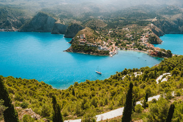 Top view to Assos village. Landmark place of Kefalonia island. Lonely white yacht at anchor in calm beautiful lagoon surrounded by pine and cypress trees. Greece