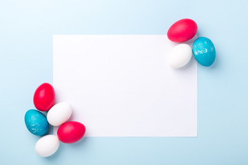 Spring mockup with Easter eggs and blank of white paper on blue background. Easter concept. Copy space. Top view