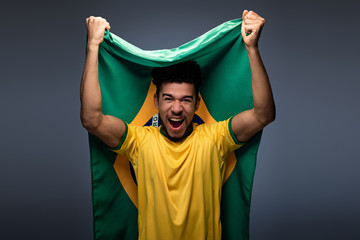 Fototapeta emotional african american football fan holding brazilian flag on grey obraz