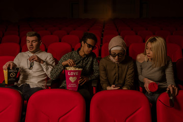 Image of laughing friends sitting in cinema watch film eating popcorn and drinking aerated sweet water.