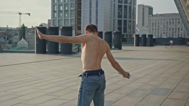 shirtless man in denim jeans sword dancing on rooftop