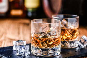 Whiskey with ice in glasses on rustic wood background. Alcohol or spirit from old barrel.
