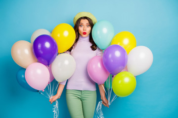 Photo of funny lady carry many colorful air balloons unexpected surprise party open mouth wear purple jumper beret cap green pants isolated blue color background