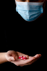 A man in a protective medical mask holds multi-colored antiviral pills in his hand during the pandemic