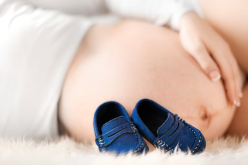 Pregnant woman belly detail  with little baby blue shoes. Pregnancy or maternity tummy concept.