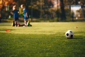 Obraz premium Soccer Horizontal Background of Sports Training for Children Team. Black White Soccer Ball on the Grass Pitch. Kids Team Standing in a Little Goal in Blurred Background