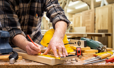 Close-up. Carpenter with pencil and carpenter's square draw the cutting line on a wooden board. Construction industry, carpentry workshop.