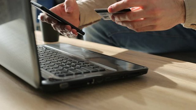 Mеn entering secure code on smartphone while shopping online using laptop with bank card