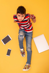 Schoolboy  sits on a yellow background surrounded by gadgets, top view.  He is faced with a choice - information overload and poor health or a happy carefree childhood.