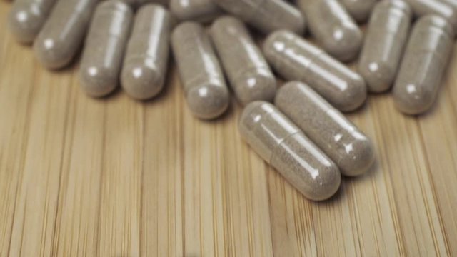 Close Up View of Natural Herbs Capsules Moving Down to Up on Wood Bamboo Background.