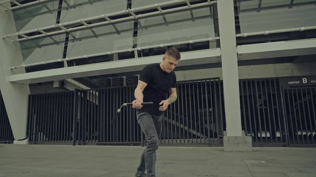 tattooed man exercising with nunchaku on street
