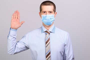 Man in shirt and medical mask holds hand at top at head level, isolated
