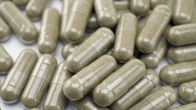 Close Up View of Natural Herbs Capsules Turning to the Left on White Background.