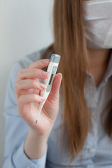 Woman in medical mask with thermometer in hand, with laptop, sitting on bed at home. Coronavirus. Business woman working from home wearing protective mask. 