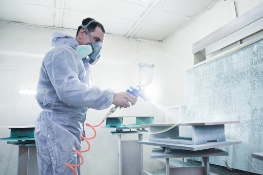 Process Of Production And Manufacture Of Wooden Furniture In Factory. Worker Man In Overalls Paints Wood With Paint Spray