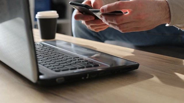 Mеn entering secure code on smartphone while shopping online using laptop with bank card