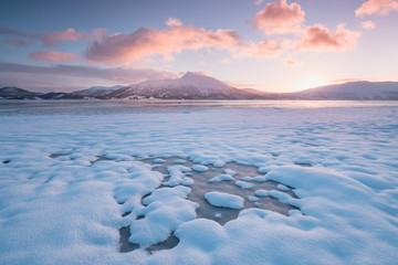 Pink early morning glow light on snow covered mountains in arctic norway, super wide panoramic scene. Scenic winter view of snowy mountain in Scandinavia. Beautiful landscape concept background.