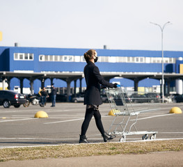 Light-skinned blonde girl in a black protective mask on her face, stands with an empty grocery cart from the market