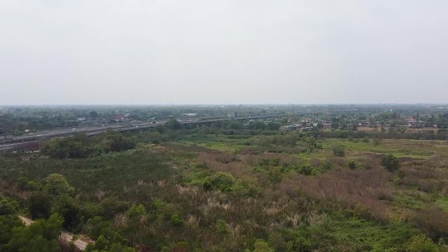 Drone Flying Over The Lush Green Field Under The Clear White Sky Of Rangsit In Pathum Thani Province, Thailand - Wide Shot