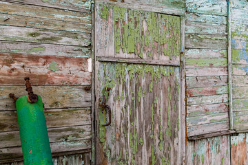 Old wooden doors on a collapsing building, a vintage barn, peeling paint, littered planks, the construction site is tilted to one side and damaged by temporary dirt