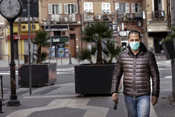 Uomo rasato con giubotto scuro indossa una mascherina protettiva chirurgica mentre cammina in contesto urbano