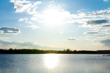 The sun in the cloudy sky. Sunset by the river near the forest.