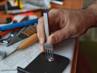  Handmade leather goods and handmade leather wallets lay on the table with crafting tools. Workflow in the workshop. Workflow in the workshop, close-up.