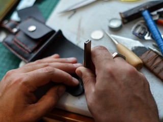  Handmade leather goods and handmade leather wallets lay on the table with crafting tools. Workflow in the workshop. Workflow in the workshop, close-up.