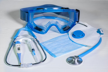 Medical protective masks, glasses and  stethoscope on a blue wooden surface. Cavid-19 coronavirus...