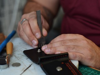Leather goods master hands and handmade leather wallets lay on table with crafting tools. Workflow in the workshop. Workflow in the workshop, close-up.