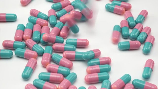 Close Up View of Blue Teal and Pink Colored Capsules Falling and Bouncing on White Background.