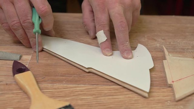 person hands with patch on finger make holes in paper template and brown wooden wing of outdated jetliner model close view
