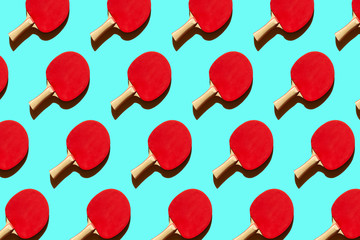 Repeating red tennis ping pong rackets with a hard shadow on a blue background, sport equipment for table tennis