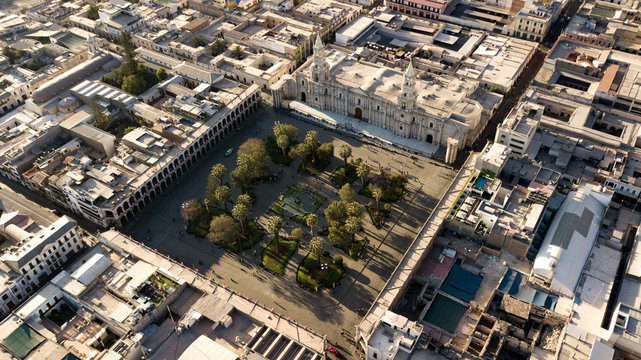 Aerial view of Arequipa's main square - UNESCO world heritage site - with cathedral made of volcanic sillar stones, geometric park and people walking during the golden hour - sun lights and shadows.