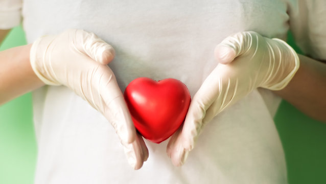 Close-up of hands in medical gloves holding red heart. Concept for charity, health insurance, love, international cardiology day, hope, donation and help during coronavirus covid-2019 pandemic