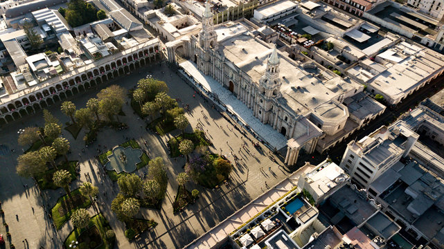 Aerial view of Arequipa's main square - UNESCO world heritage site - with cathedral made of volcanic sillar stones, geometric park and people walking during the golden hour - sun lights and shadows.