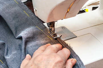 Elderly woman sews denim on a home sewing machine. Grain effect