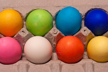 2 rows of orange, green, blue, pink, white, red and yellow dyed eggs arranged in cardboard egg carton