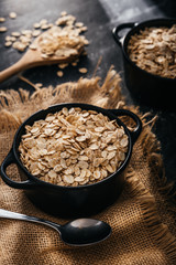 Top view of two black bowls and spoon with raw oatmeal on a black background. Breakfast with fibers...