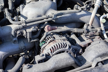 Dusty details of a flat-four (boxer) car engine compartment under the open hood. Alternator and intake manifold