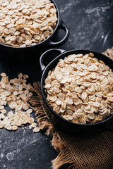 Two black bowls and spoon with raw oatmeal on a black background. Breakfast with fibers for a balanced diet. Oat photo