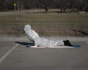 Life during epidemic. Woman in a protective suit, mask and gloves makes yoga exercises in empty city park. Summer season, selective focus. Lifestyle and sport during coronavirus (covid-19) pandemic.