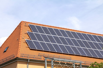Close-up of a house roof with a solar panels on top, on a blue sky