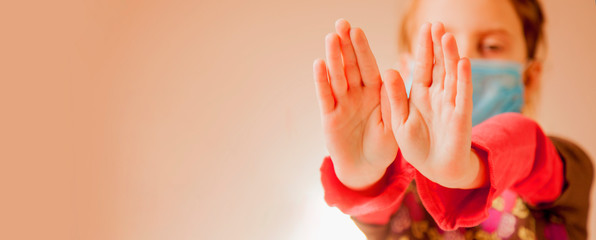 Portrait of cute little child girl in blue medical protective mask showing gesture stop. Selective focus on hands. Free space for design.