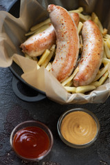 Close-up of roasted chicken sausages with french fries in a cast-iron pan, selective focus, vertical shot