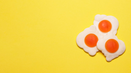 Widescreen photo of three jelly eggs in the lower right on a yellow background, flat lay.