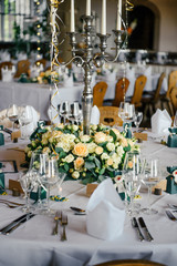 Decorated tables for guests at the wedding, there are candlestick, wine glasses, plates, napkins, tablecloth, fresh flowers