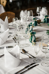Decorated tables for guests at the wedding, there are wine glasses, plates, napkins, tablecloth, bonbonierre, spoons, forks, knifes